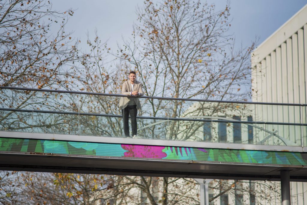 Über uns: Markus Thellmann von HRE steht auf einer bunten Glasbrücke